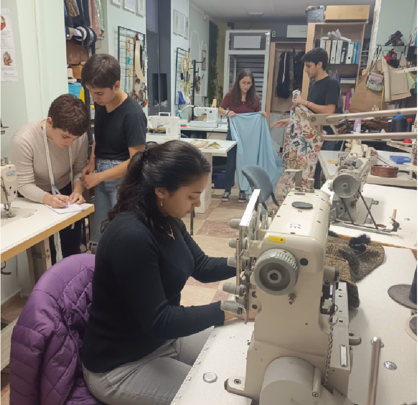 Grupo de estudiantes trabajando con máquinas de coser en un taller de clases de confección textil.